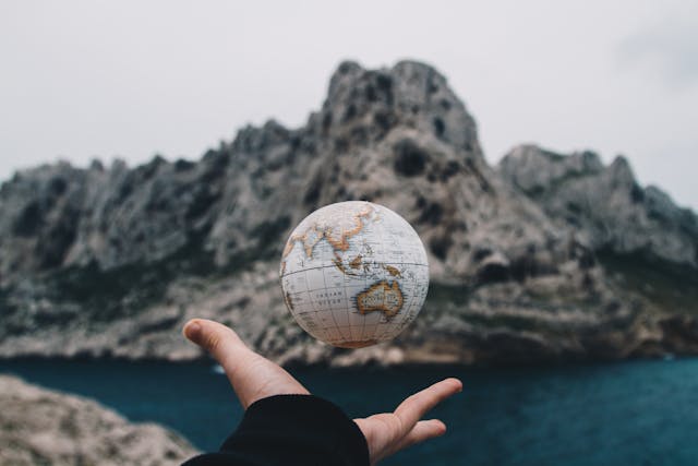 A globe thrown up by a person's left hand with a beach rocks on the background